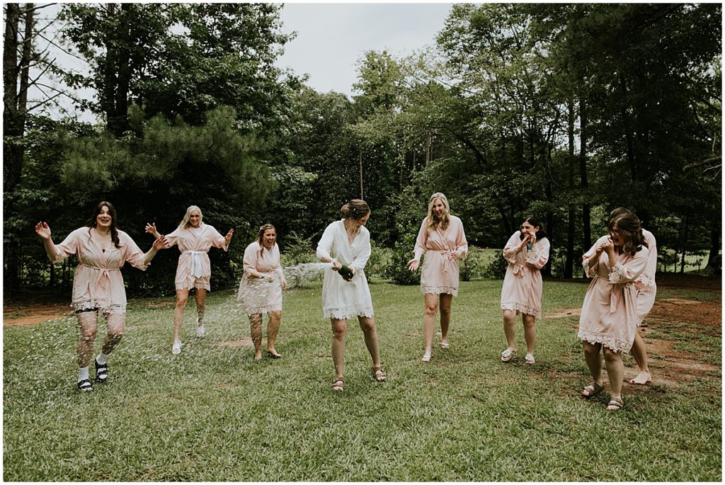Bride popping champagne with her bridesmaids in the grounds of Koury Farms, Auburn Wedding Venue.