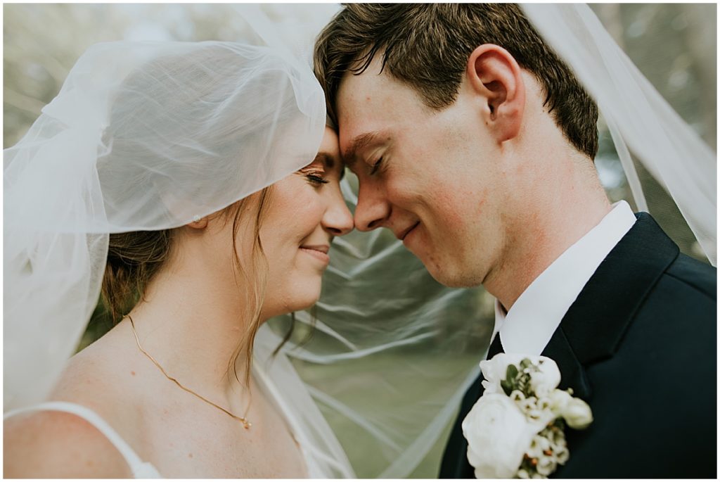 Bride and groom under a wedding veil smiling at each other with eyes closed