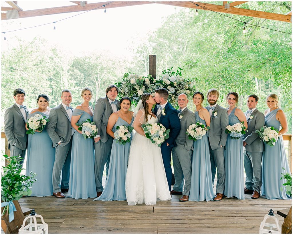 Bride and groom kissing surrounded by bridal party at North Georgia Barn Wedding Venue