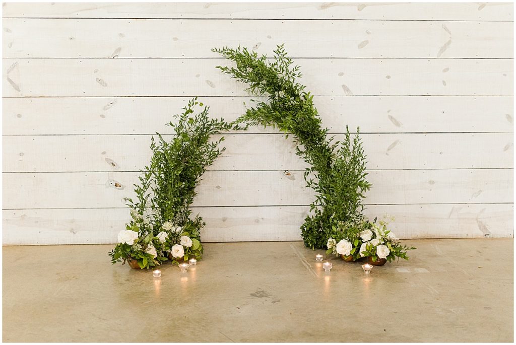 Wedding arbor in green florals with ivory roses and candles placed at the bottom