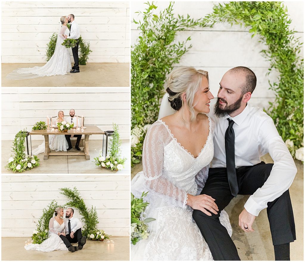 Bride and groom posing in front of greenery and ivory floral arbor and wedding table, with a rustic elegant vibe