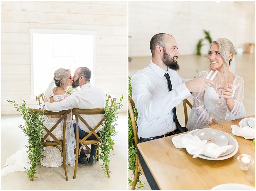 Bride and groom clinking glasses and sharing a kiss at the table at koury farms rustic and elegant wedding and event venue.
