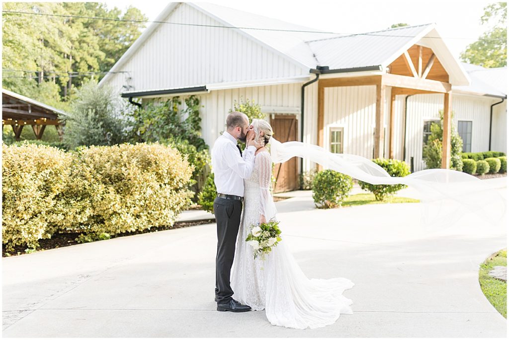 Bride and groom kissing in front of the main entrance at Koury farms, a rustic, elegant wedding and event venue