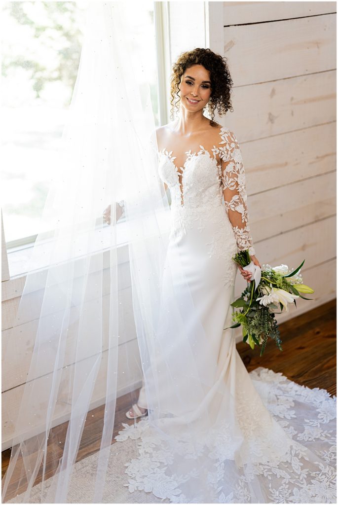 Bride standing by a window in intricate lace dress