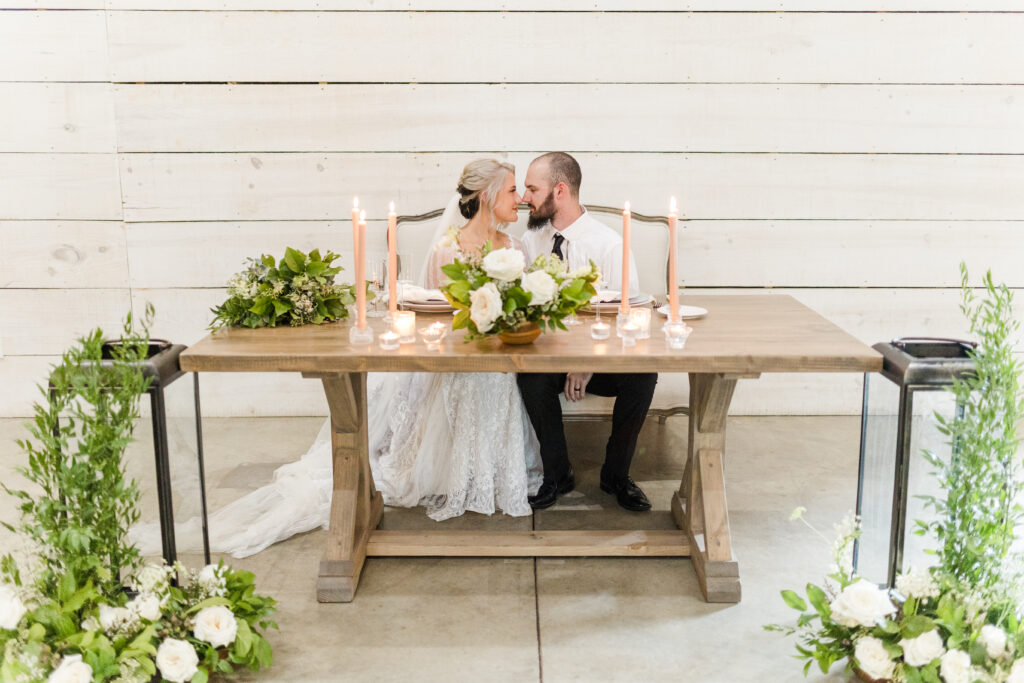 Bride and groom at sweetheart table decorated with greenery and white florals
