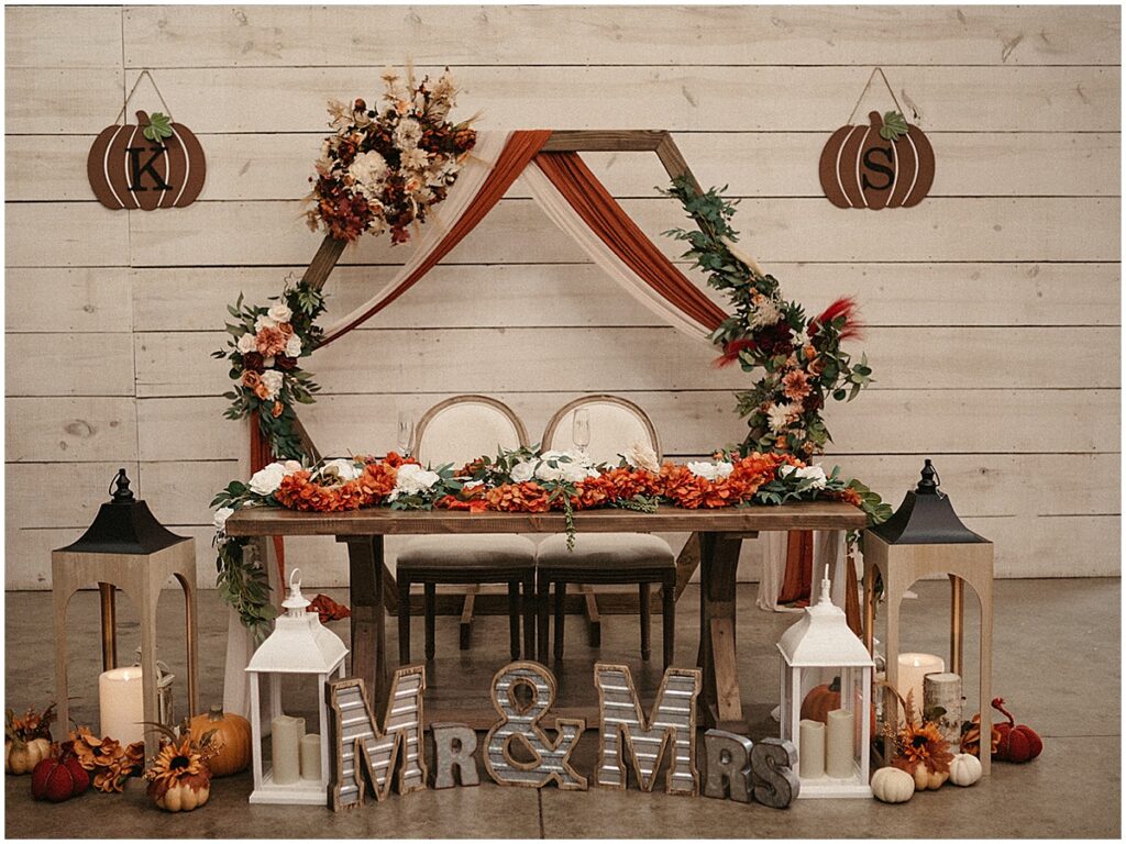 sweetheart table decorated with lanterns, pumpkins, fall decor