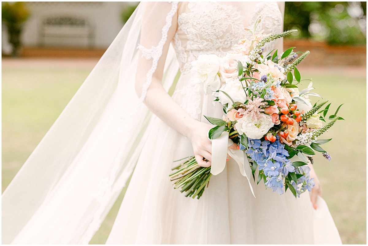 Bride carrying large bouquet of blue, white and orange florals designed by Flori Weddings