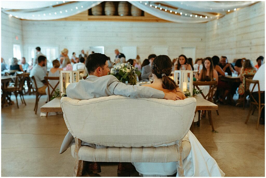 bride and groom sitting in sweetheart chair looking at wedding reception