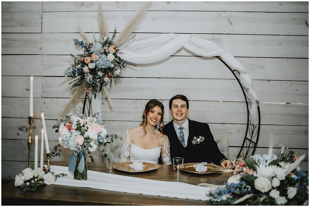 Bride and groom at sweetheart table with blue and white florals and pampas grasses for a whimsical winter wedding at Koury Farms.