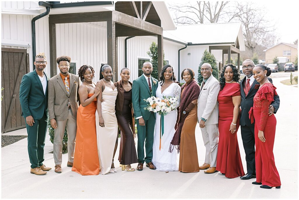 Bride and groom with guests wearing bright orange, red and brown attire