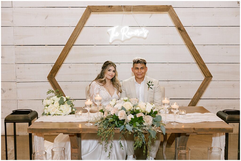 Bride and groom sitting at sweetheart table with candles and ivory florals