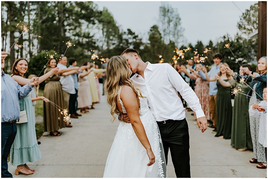 Bride and groom kissing at sparkler exit at olive, black and gold wedding