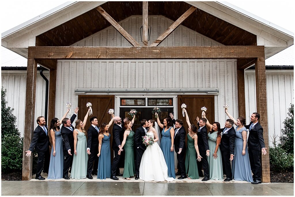 Bride and groom kissing surrounded by wedding party with hands in the air at succulent inspired wedding