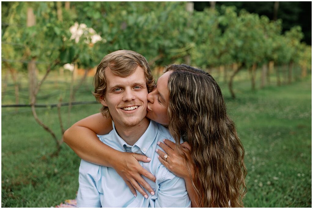 Woman kissing man at romantic vineyard engagement session at Koury Farms