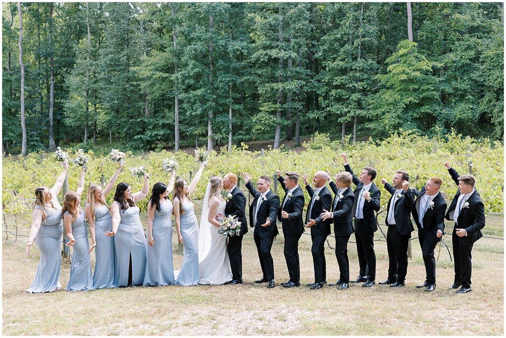 Bride and groom kissing in the middle with wedding party cheering them on