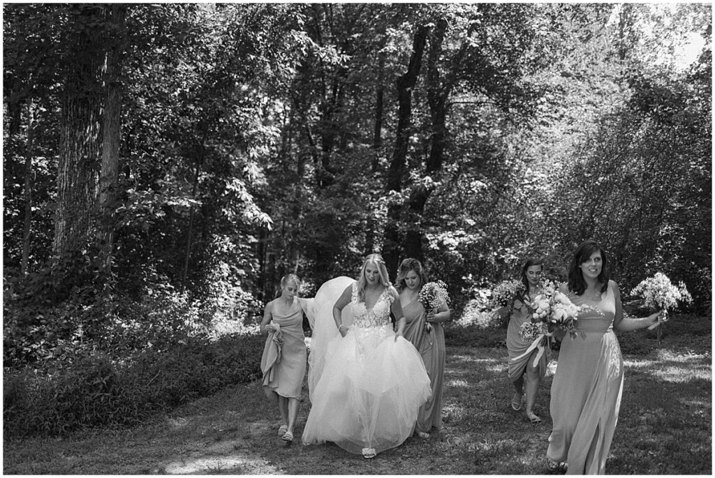 Bride walking with bridesmaids holding her dress for elegant fairytale wedding at Koury Farms