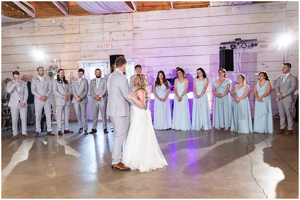 Bride and groom first dance with wedding party looking on