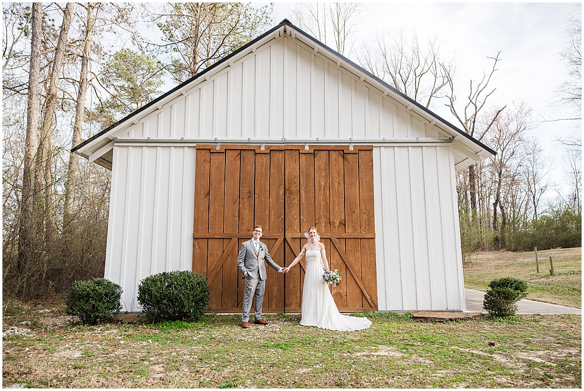 Couple standing outside white barn at March wedding at Koury Farms