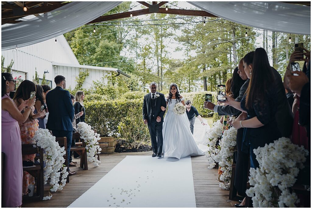 bride walking down the aisle with her father and groom looking on